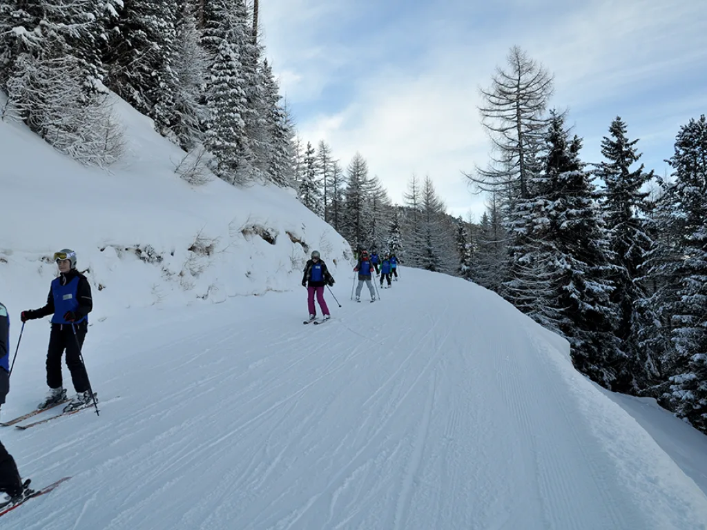 Skifahrende auf einer schmalen Piste zwischen Schneewänden.